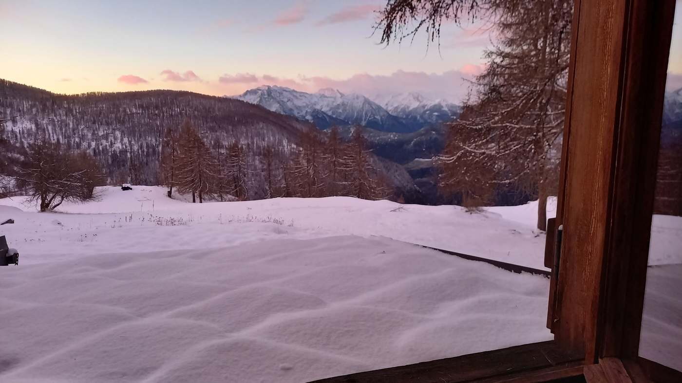 Vue depuis une fenêtre du chalet sur le jardin enneigé au crépuscule.