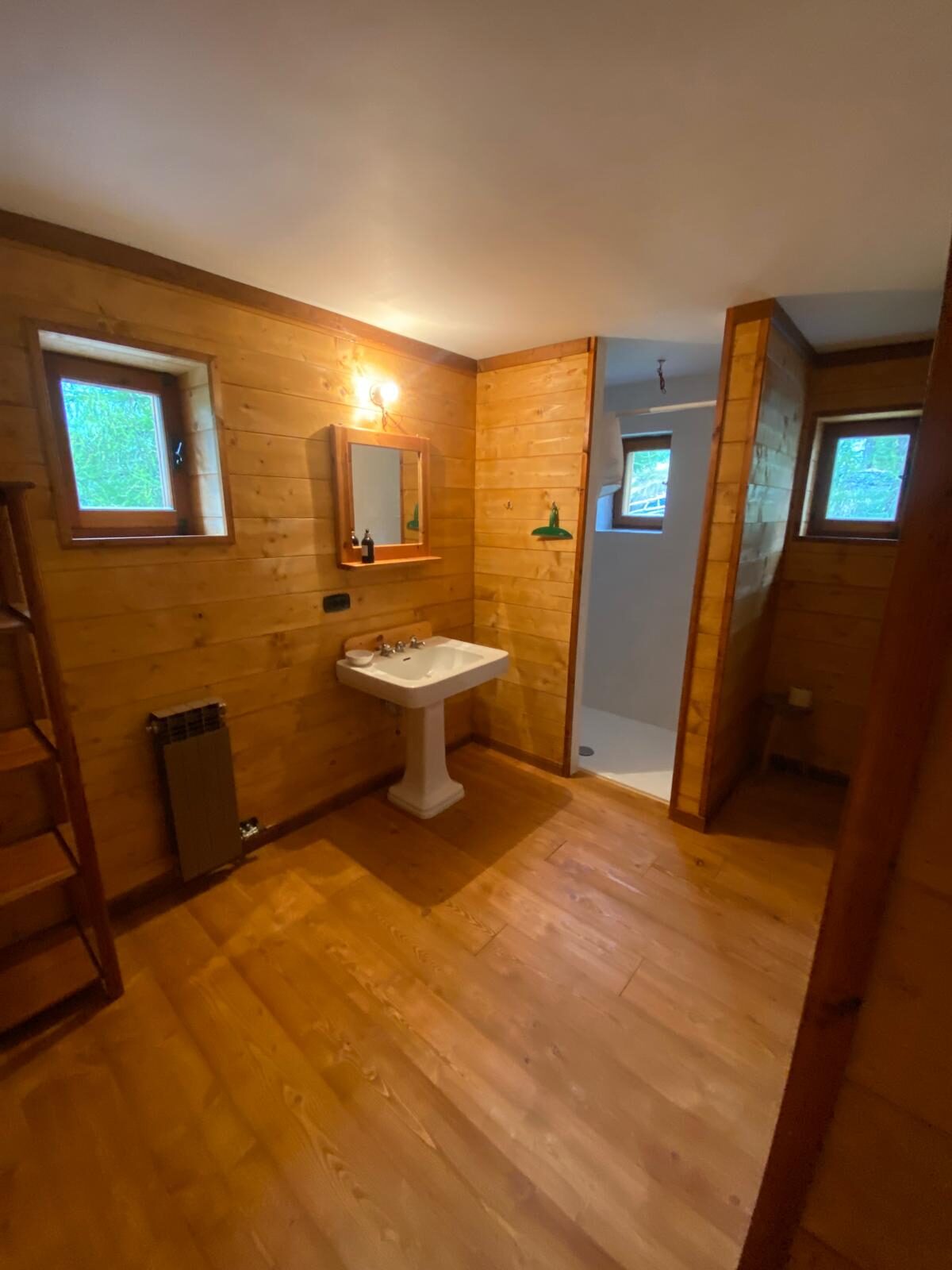 Salle de bain lambrissée du 1er étage avec lavabo, douche et fenêtre.
