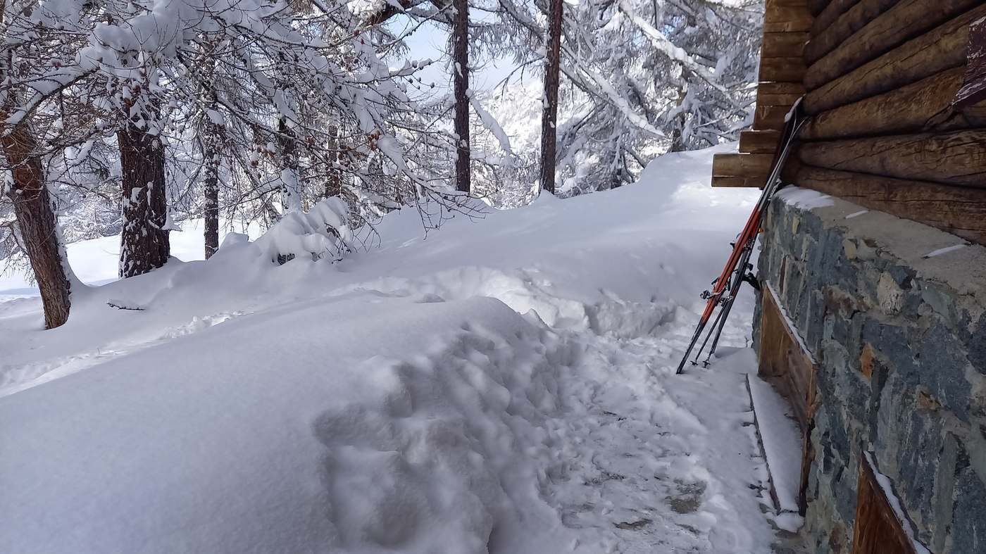 Skis posés contre la façade du chalet enneigée.