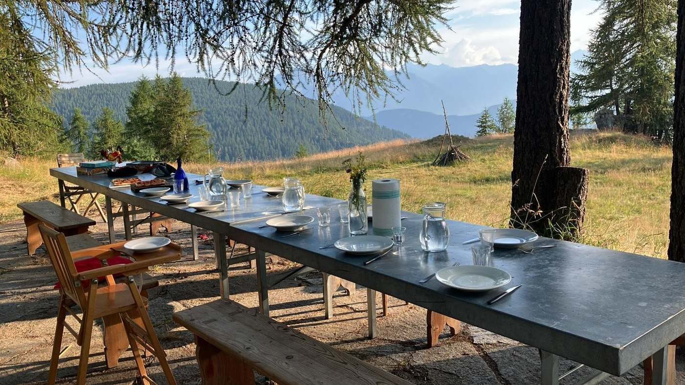 Longue table dressée en extérieur face aux montagnes, à l'heure du dîner.
