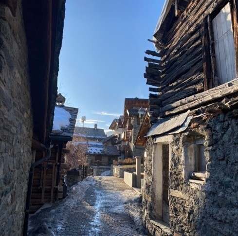 Ruelle piétonne de Chamois entre maisons de pierre, sous la neige.