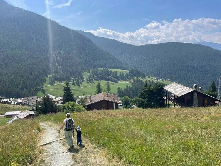 Sentier menant à Chamois à travers les prairies, promeneurs au loin.
